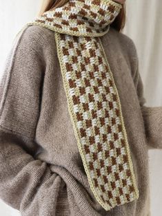 a woman wearing a knitted scarf in brown and white checkerboard pattern, standing with her hands on her hips