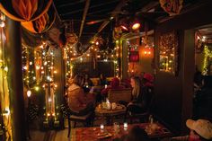 people sitting at tables in a restaurant with lights strung from the ceiling and decorations on the walls