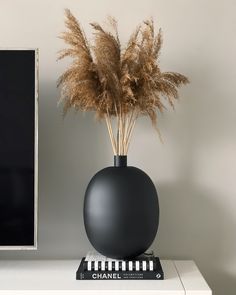 a black vase sitting on top of a white table next to a computer monitor and keyboard