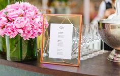 pink flowers are in vases on a table with menu cards and wineglasses