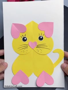 someone holding up a paper cut out of a cat with pink ears and paws on it