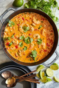 a skillet filled with shrimp and rice next to limes, cilantro, and tortilla chips