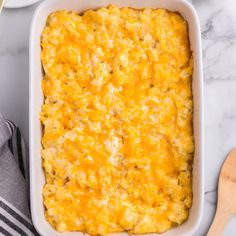 a casserole dish filled with cheese on top of a white counter next to a wooden spoon