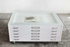 an open book is sitting on top of a white table with drawers and wheels in front of it