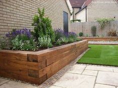 a wooden planter filled with lots of plants next to a brick wall and green grass