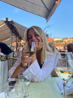 a woman sitting at a table with a glass of wine in front of her face