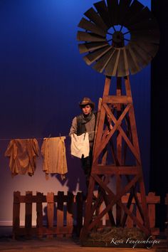 a man standing next to a windmill on top of a wooden structure with clothes hanging from it