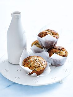 four muffins on a white plate next to a bottle and cupcake tin