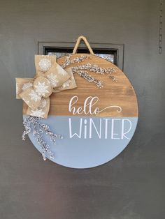 a wooden sign that says hello winter hanging on the front door with ribbon and snowflakes