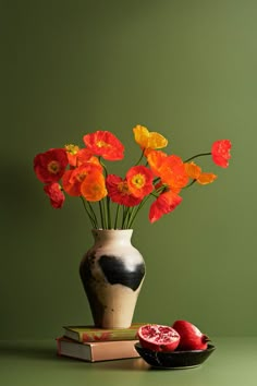 a vase filled with red and yellow flowers next to a bowl of pomegranates