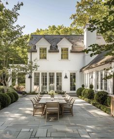 an outdoor dining table and chairs in front of a large white house with lots of windows