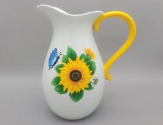 a white pitcher with sunflowers and butterflies painted on the side, sitting against a gray background