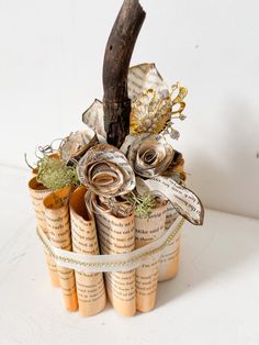 an arrangement of rolled up book pages and flowers in a basket with ribbon tied around it