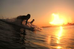 a person riding a surfboard on top of a wave in the ocean at sunset