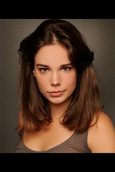 a beautiful young woman with long hair posing for a photo in front of a gray background