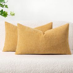 two yellow pillows sitting on top of a white couch next to a potted plant