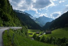 a scenic road in the mountains with houses on each side and green grass to the left