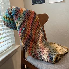 a multicolored blanket sitting on top of a wooden chair next to a window