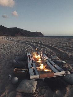 a table set up on the beach at night with people standing around and lighting candles