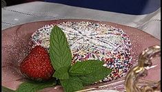 a strawberry cake with sprinkles and a green leaf on the plate next to it