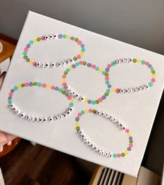 a person holding up a white canvas with colorful beads in the shape of an olympic symbol