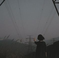 a woman standing under power lines in the dark with her hand up to the sky