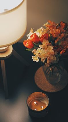 a vase with flowers on a table next to a lit candle and a lamp shade