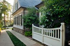 a white picket fence in front of a house with trees and bushes on the side