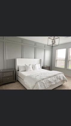 a large white bed sitting in a bedroom next to two nightstands and a window