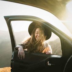 a woman wearing a hat sitting in the back of a car with her arms out