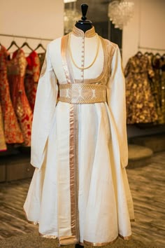 a mannequin dressed in white with gold trims stands next to other dresses