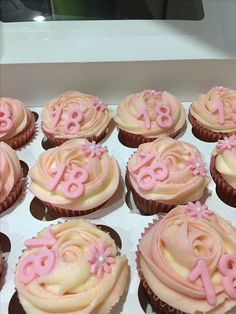 cupcakes with pink frosting and decorated numbers in a white box on a table