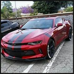 two cars are parked side by side in a parking lot, one is red and the other is black