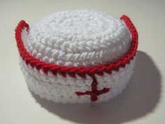 a white crocheted hat with red trim and a cross on it, sitting on a table