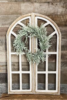 an old window with a wreath on the front and side panels, against a wooden wall