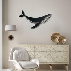 a living room with a white chair and a black whale wall hanging on the wall