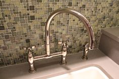 a white sink sitting under a faucet next to a green tile backsplash