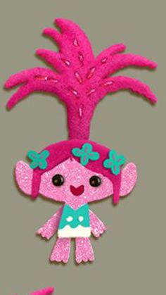 a pink and green doll with flowers on it's head, sitting in front of a