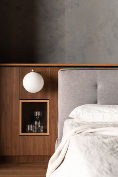 a bed with white linens and pillows in a dark room next to a wooden headboard