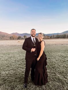 a man and woman in formal wear posing for a photo on the grass with mountains in the background