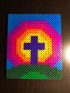 a cross made out of perforated plastic beads on top of a wooden table