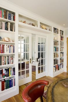 a living room filled with lots of books on top of white book shelves next to a wooden floor