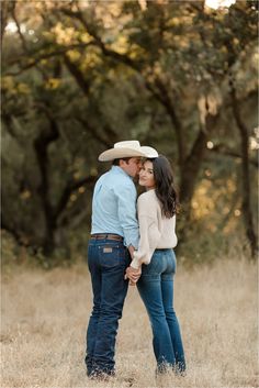 a man and woman are standing in the grass with their arms around each other while looking at each other