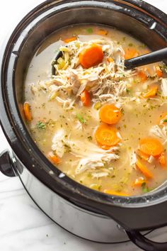 a crock pot filled with chicken and carrots on top of a marble counter