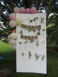 a sign with flowers and balloons attached to it that says class of boba in front of a tree