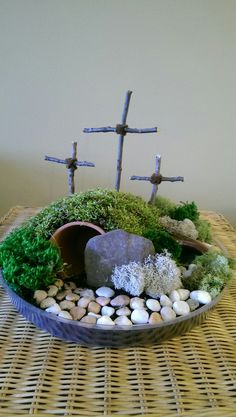 a bowl filled with rocks and moss next to a wooden cross on top of a table