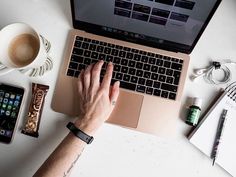 a person typing on a laptop computer next to a cup of coffee and cell phone