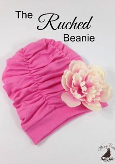 the ruched beanie is pink with a flower on it and text overlay reads,