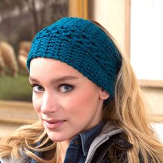 a woman wearing a knitted headband in front of a painting and looking at the camera