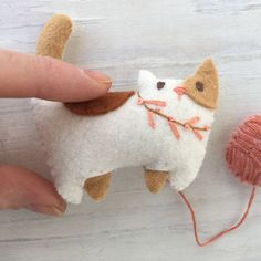 a hand is holding a needle - felt cat ornament next to a ball of yarn